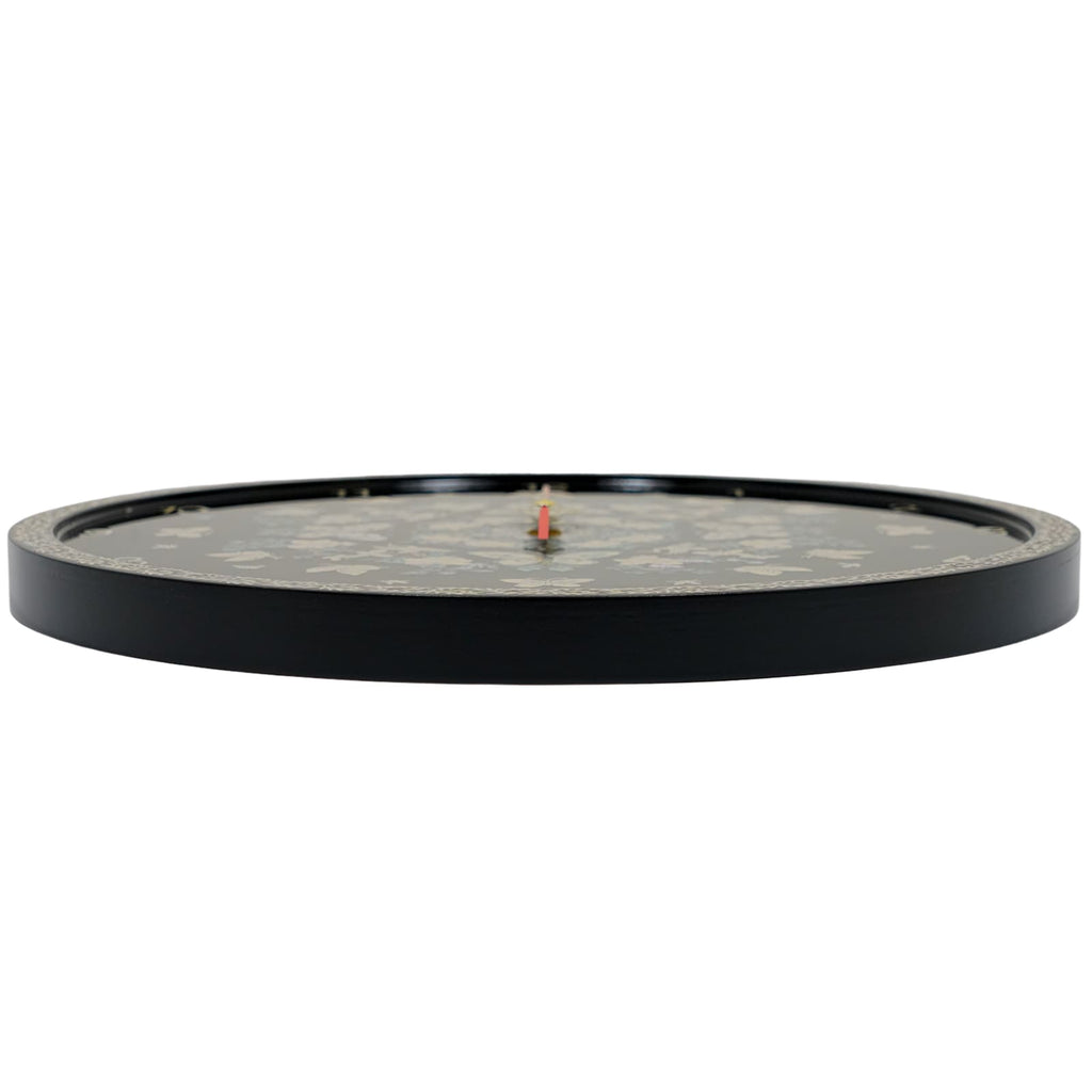 Side view of a round wall clock with a black face featuring subtle "Mother of Pearl" flower designs. The clock has a black exterior rim and a red central hand. The edge of the face has a patterned border.