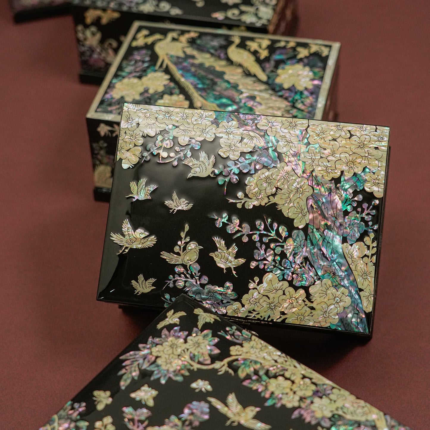 An intricately designed jewelry box with mother-of-pearl inlays featuring birds and flowers is depicted, showcasing reflective and colorful surfaces.