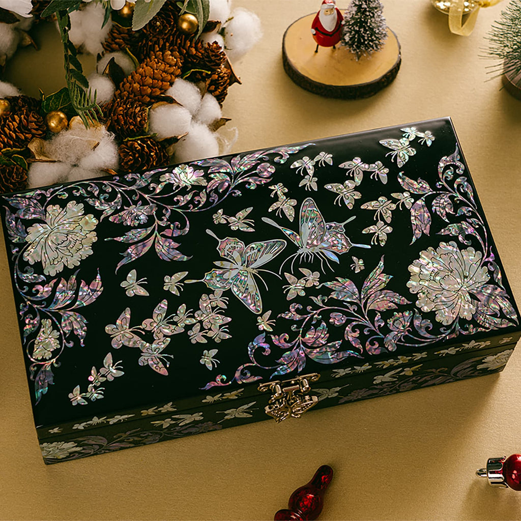 A black lacquered jewelry box with mother of pearl butterfly and floral design, set against a festive background with holiday decorations.