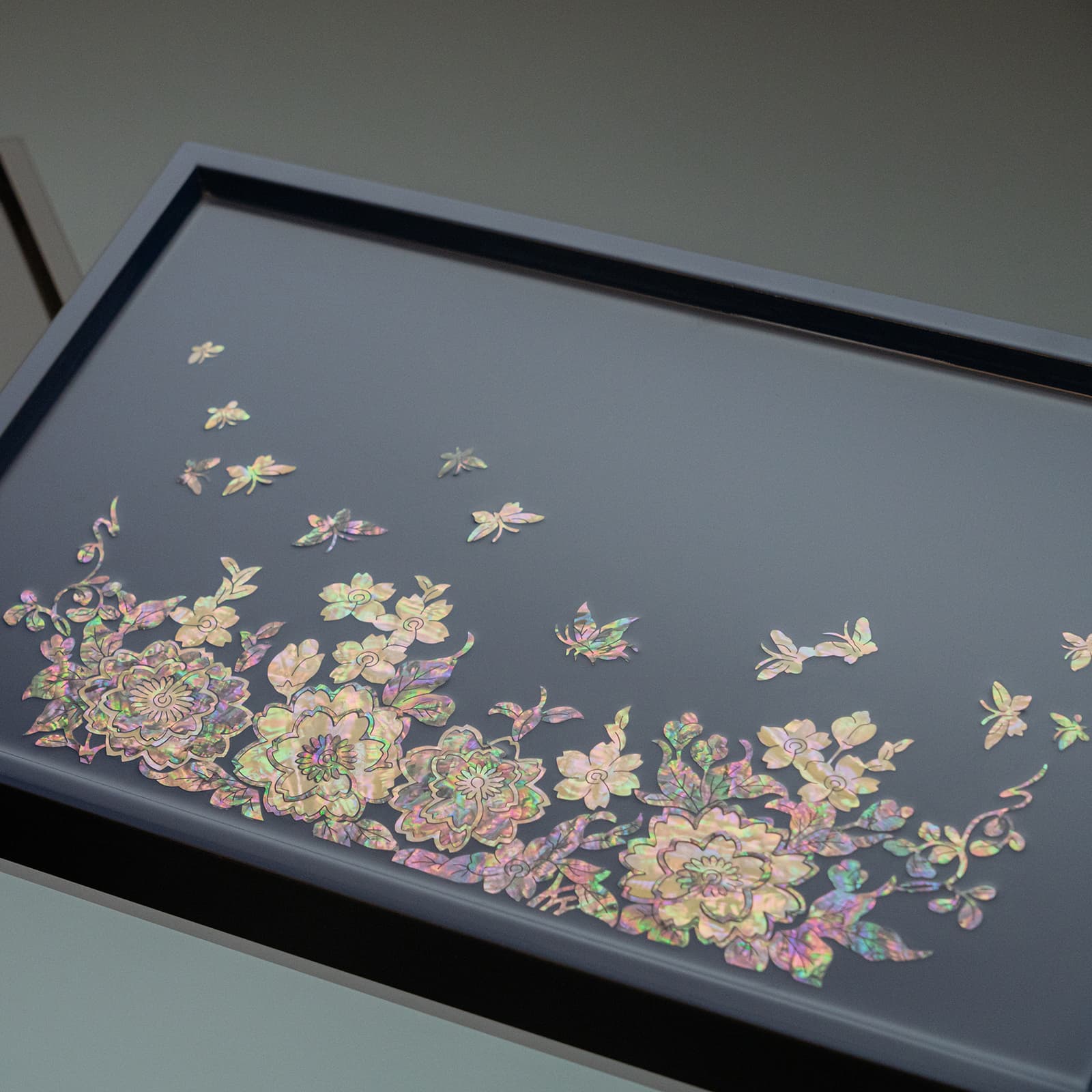 A close-up of a dark blue tray featuring a radiant Mother of Pearl floral and butterfly design, with a high-contrast edge visible against a lighter background.