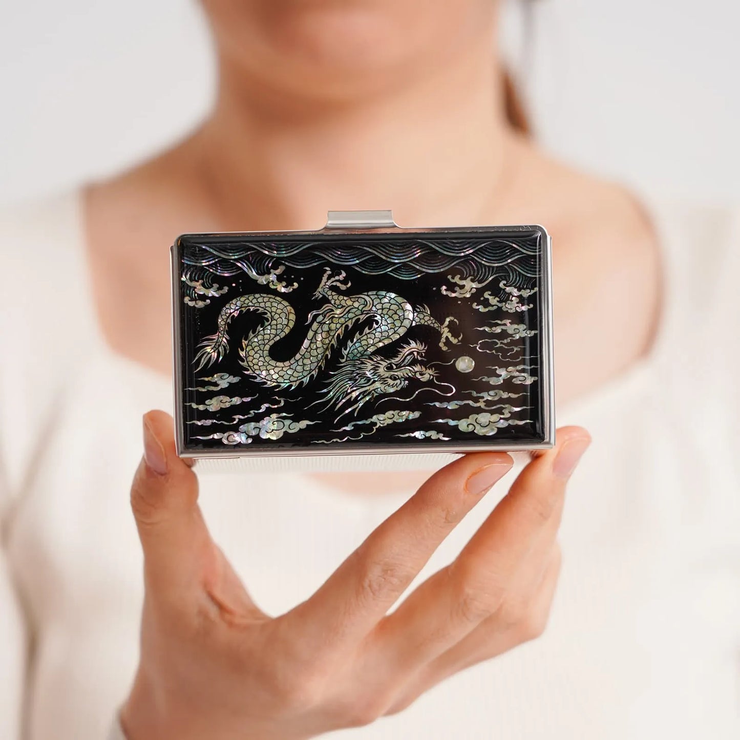 A decorative box featuring a dragon surrounded by clouds and waves, held by a person in a white top