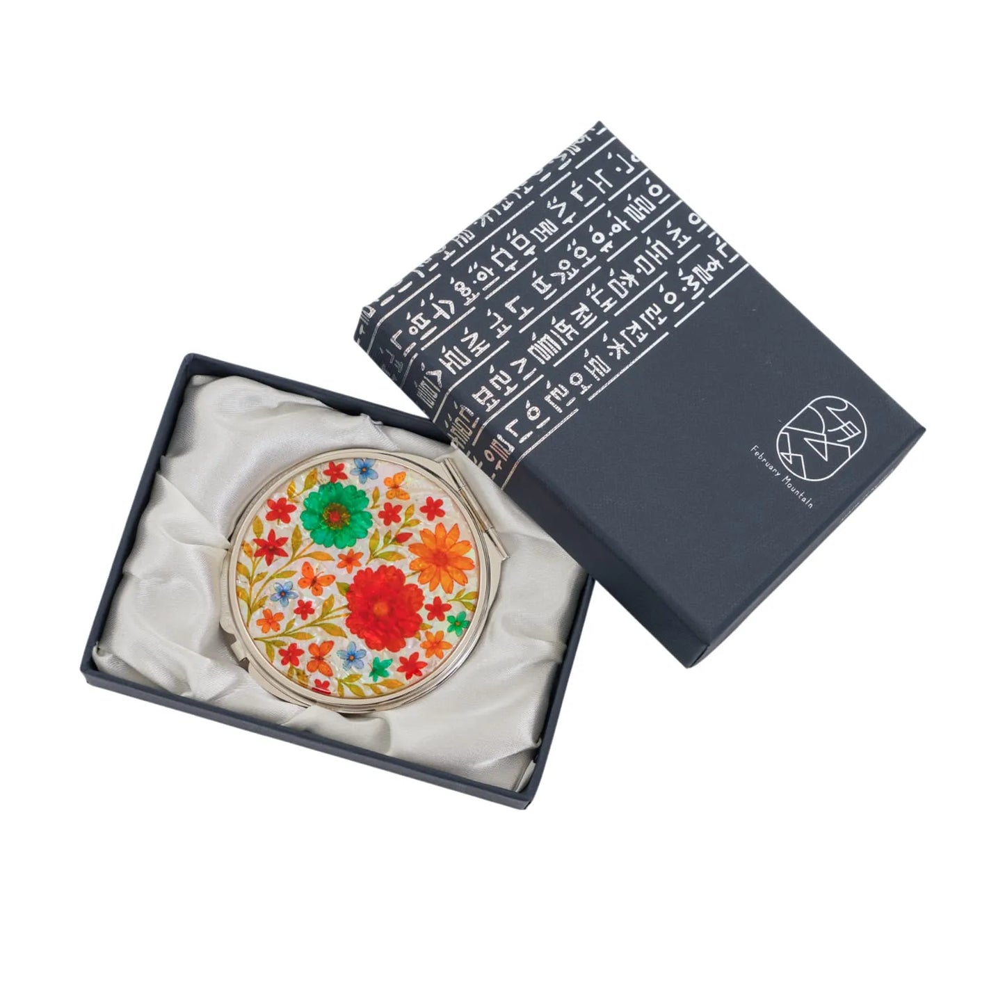 A decorative compact mirror with colorful floral design in a black box with white script and logo.
