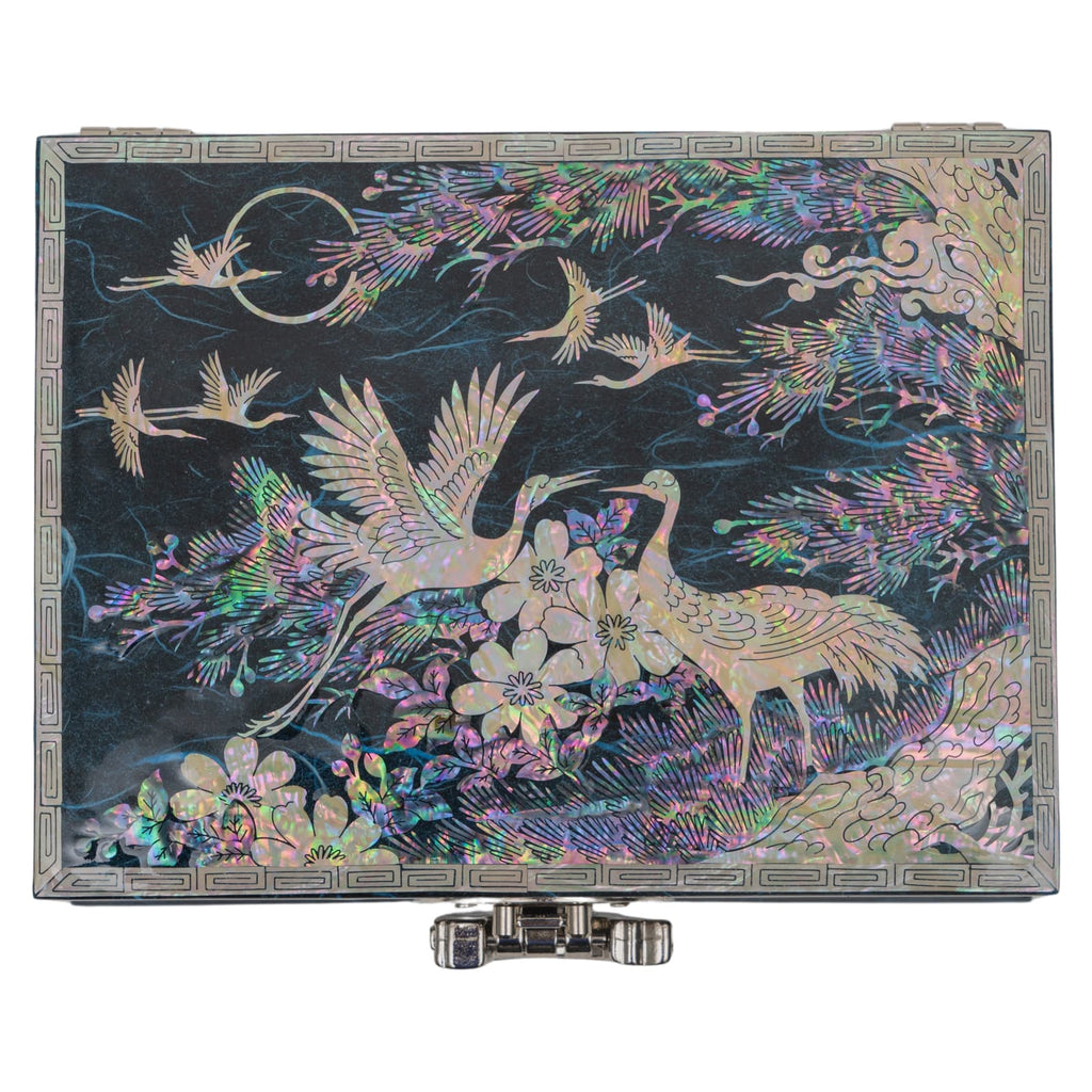 A flat-lay view of a closed mother-of-pearl inlaid box, featuring vibrant crane and floral motifs on a dark background with a metallic front latch.