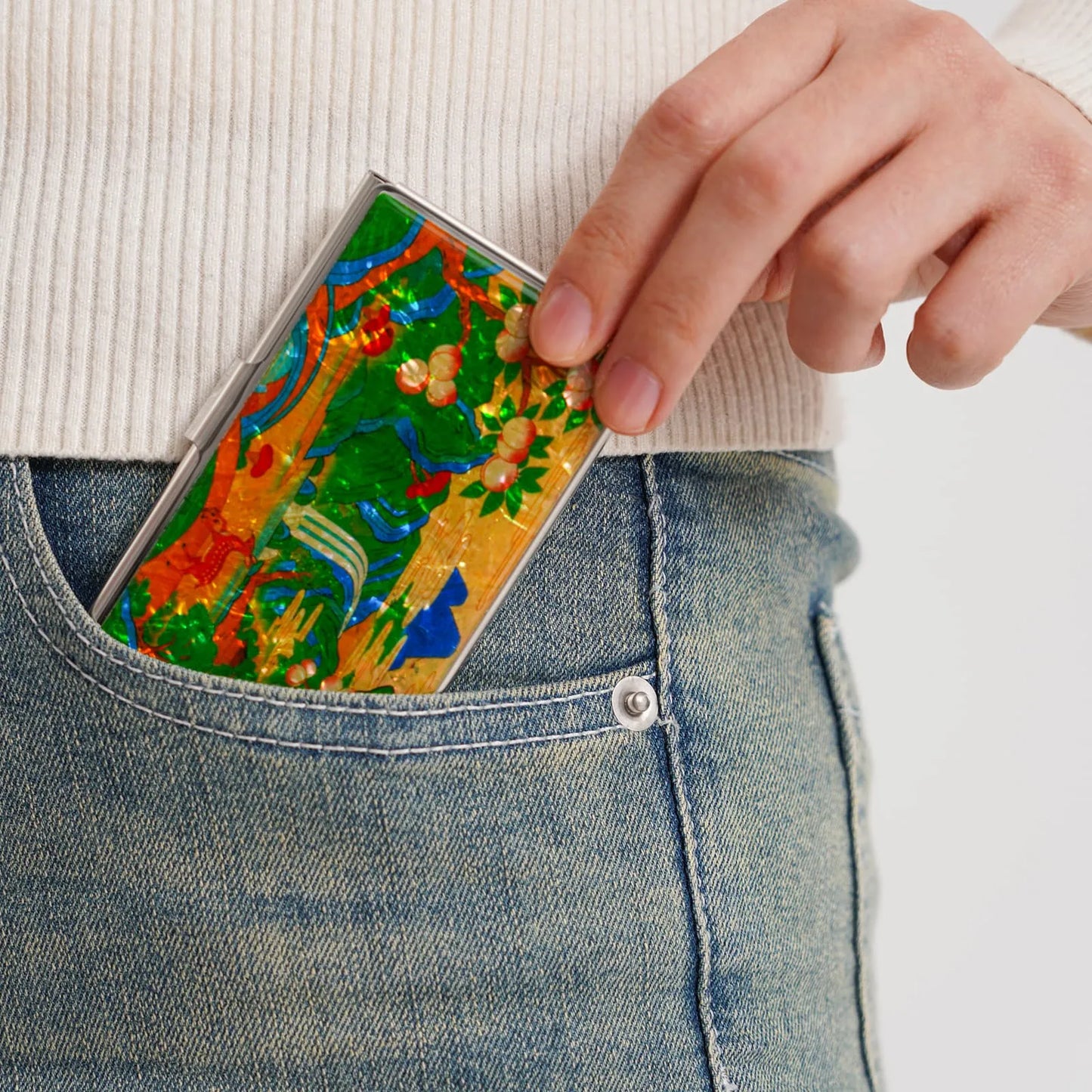 A hand places a colorful case with floral and abstract patterns into the front pocket of blue jeans