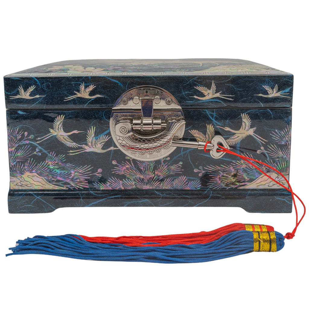A mother-of-pearl inlaid box with crane and floral designs, a metallic latch, and a red string with a blue and red tassel attached, on a dark blue background.