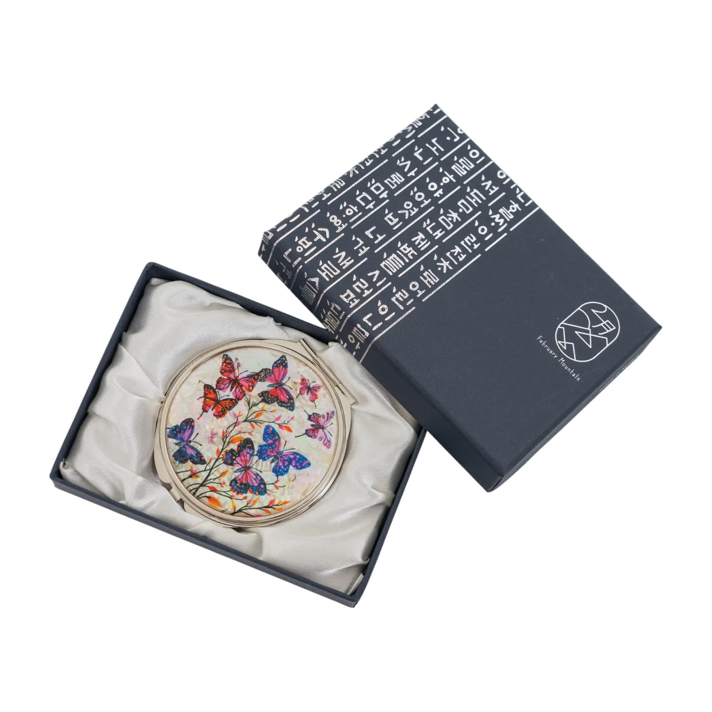 An open dark blue box lined with white satin fabric, containing a round decorative item with a colorful design featuring butterflies and flowers. The box ha
