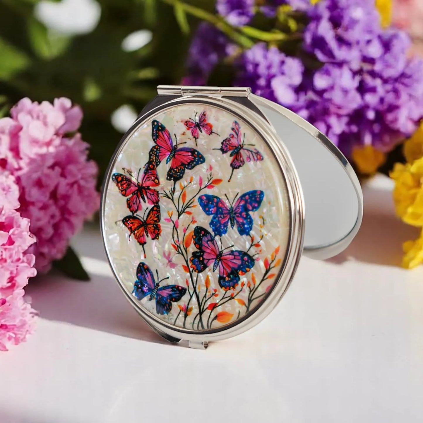 An open round compact mirror with an iridescent cover featuring colorful butterflies and delicate flowers, surrounded by vibrant pink, purple, and yellow bl