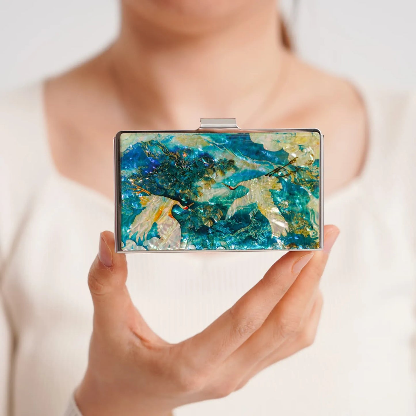 A person holds a decorative rectangular clutch featuring blue, green, and yellow abstract patterns