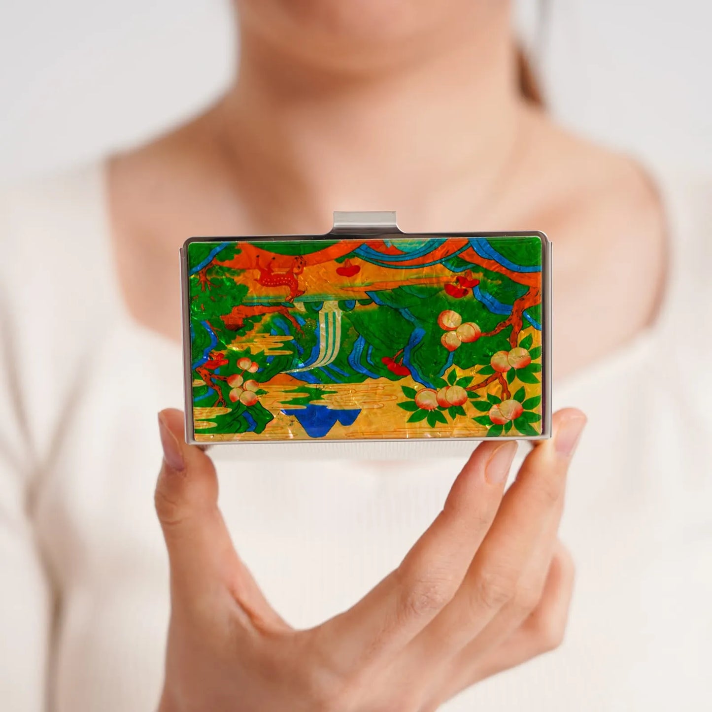 A person holds a decorative rectangular object with a vibrant floral and abstract design on its surface