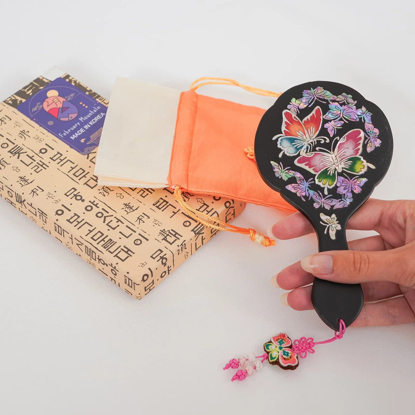 Black hand mirror with butterfly design, orange pouch, and Korean box