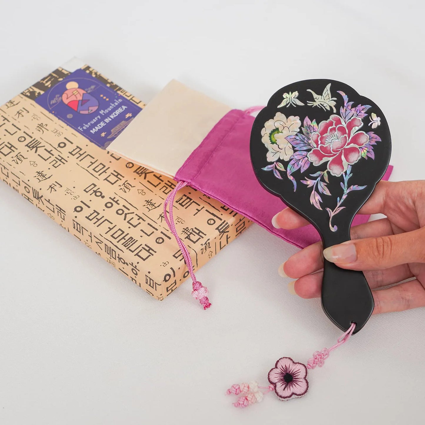 Black hand mirror with red peony and butterflies, next to purple pouch and box
