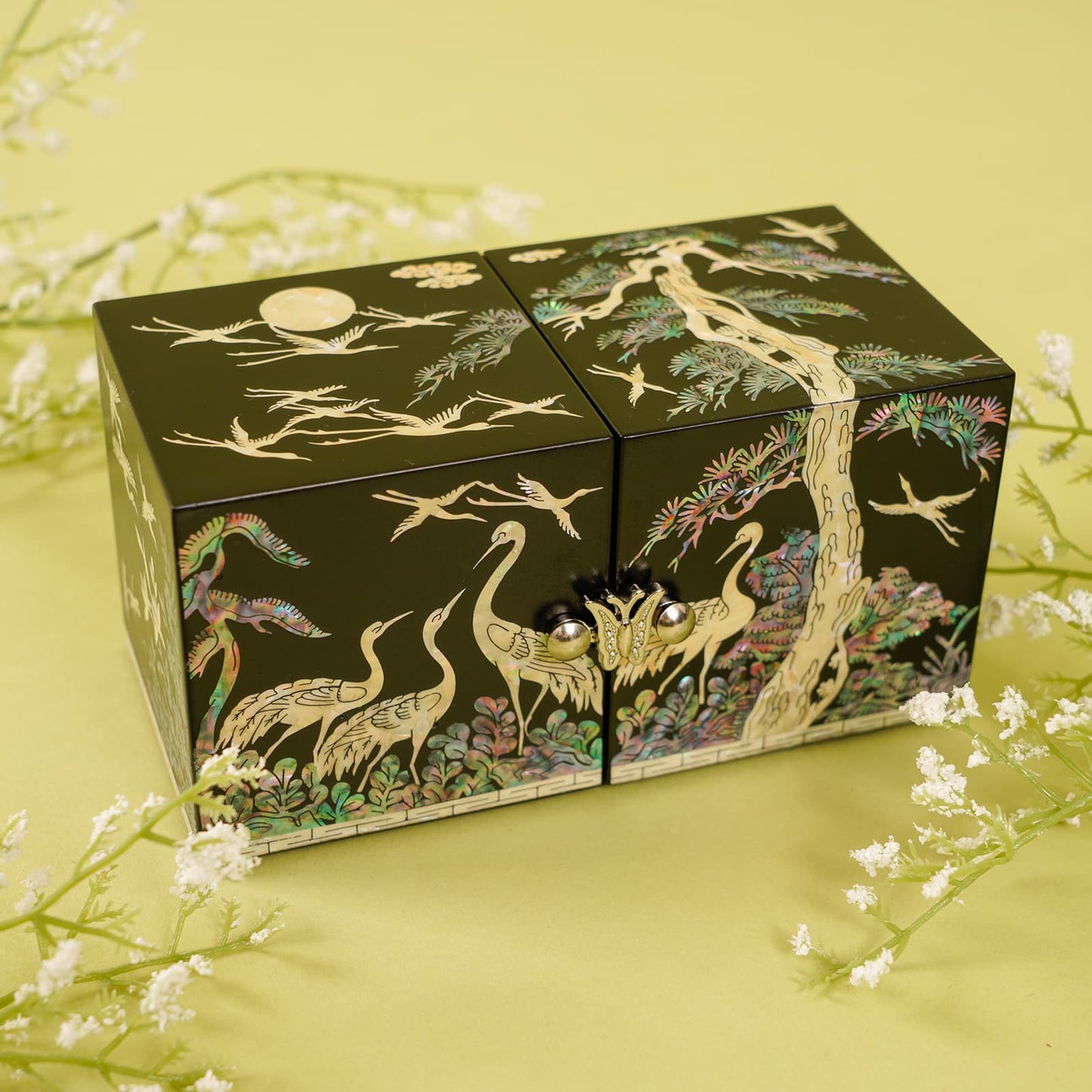 Black lacquer jewelry box with cranes and pine inlay, displayed on a soft yellow floral background