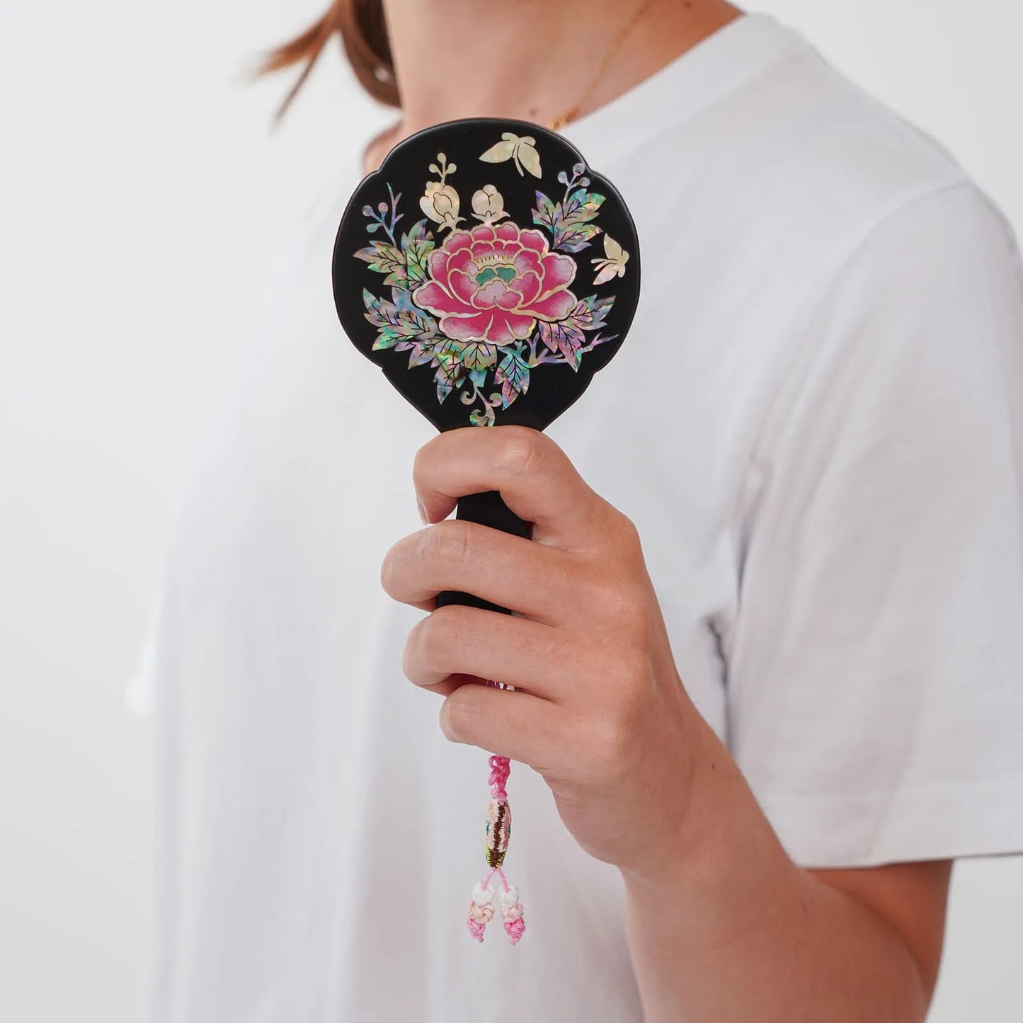 Black mirror with floral inlay and butterfly tassel, held in hand