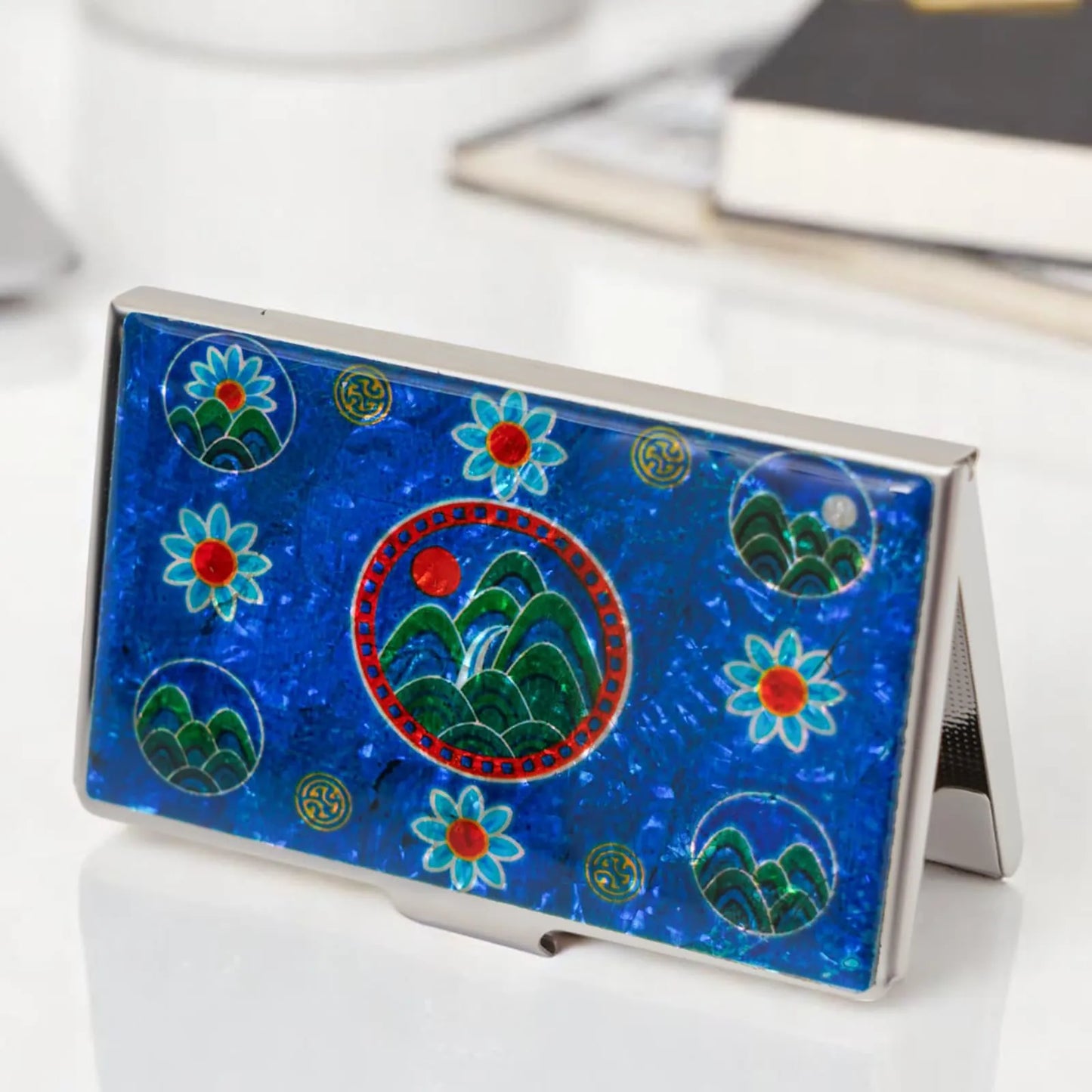Blue mother-of-pearl card case standing upright on desk with books
