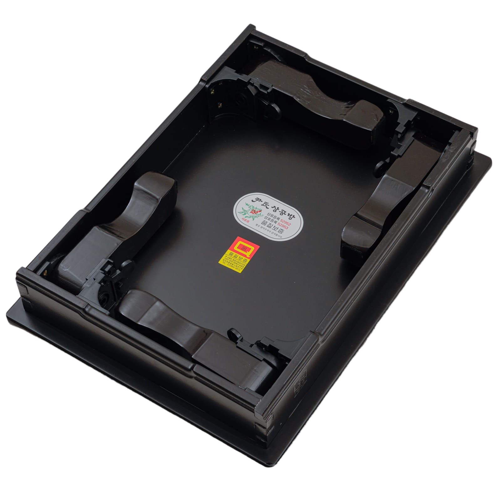 Bottom view of a black lacquered tray with foldable legs, showing quality assurance stickers and certification labels.