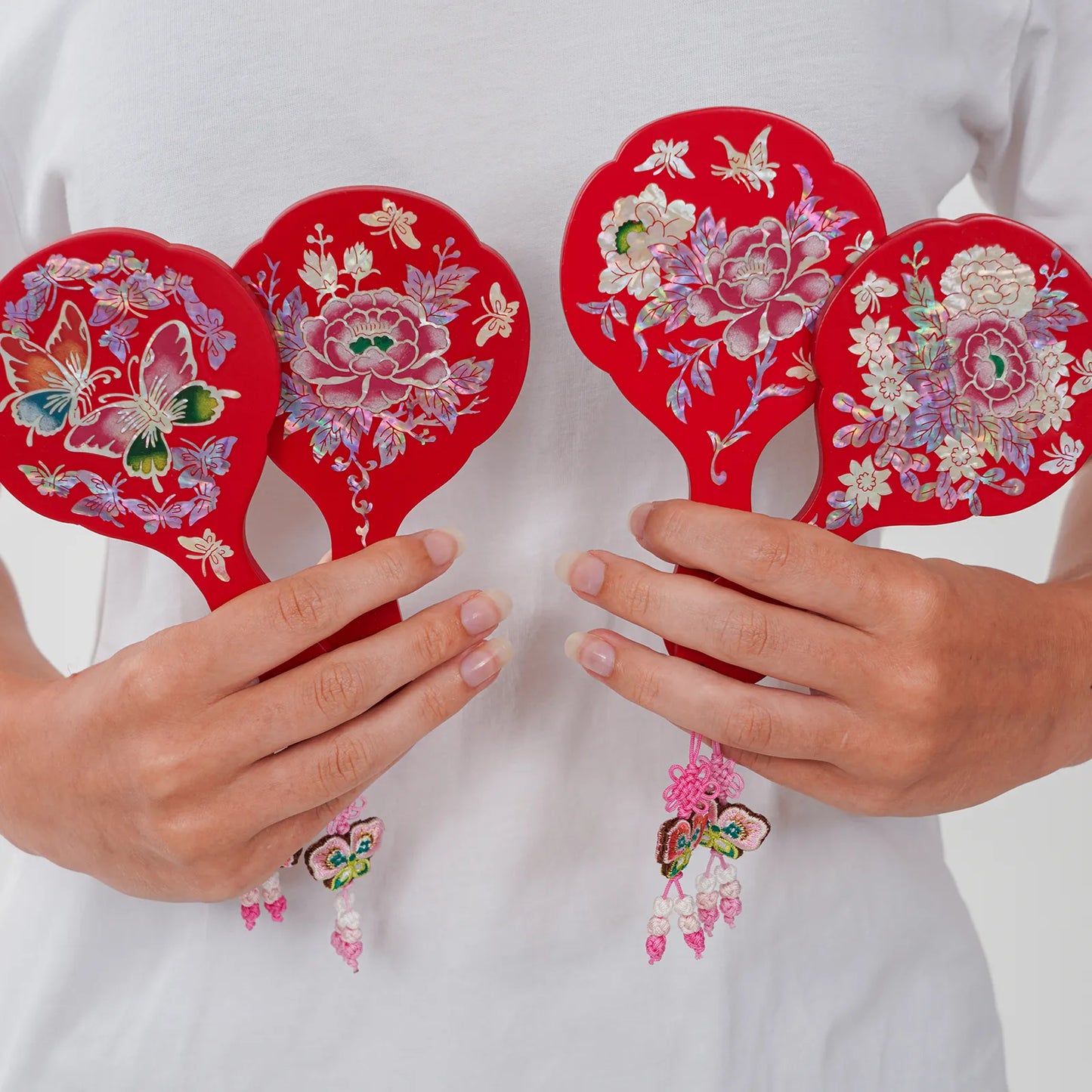 Four red floral and butterfly hand mirrors with tassels held in hands