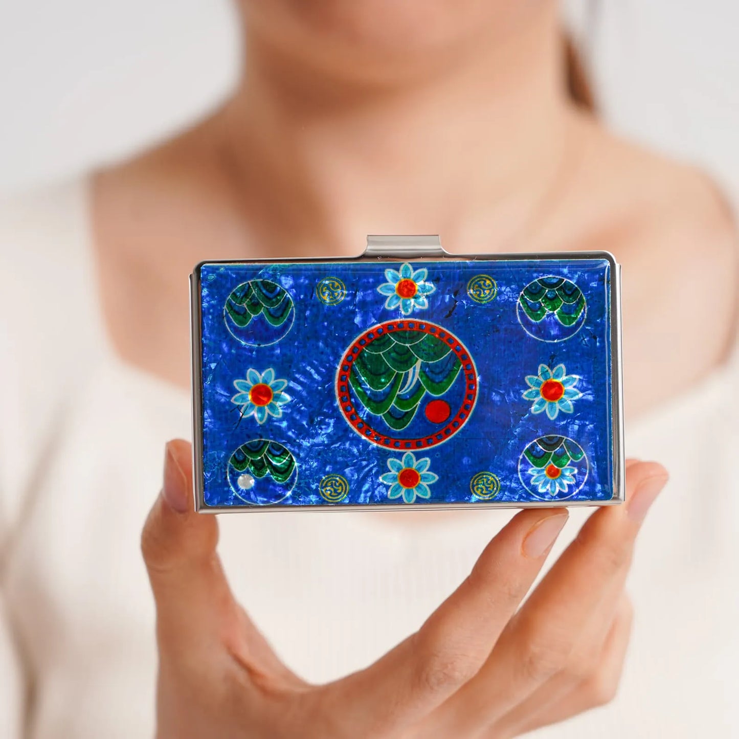 Hand holding card case with mountain and flower pattern on deep blue background