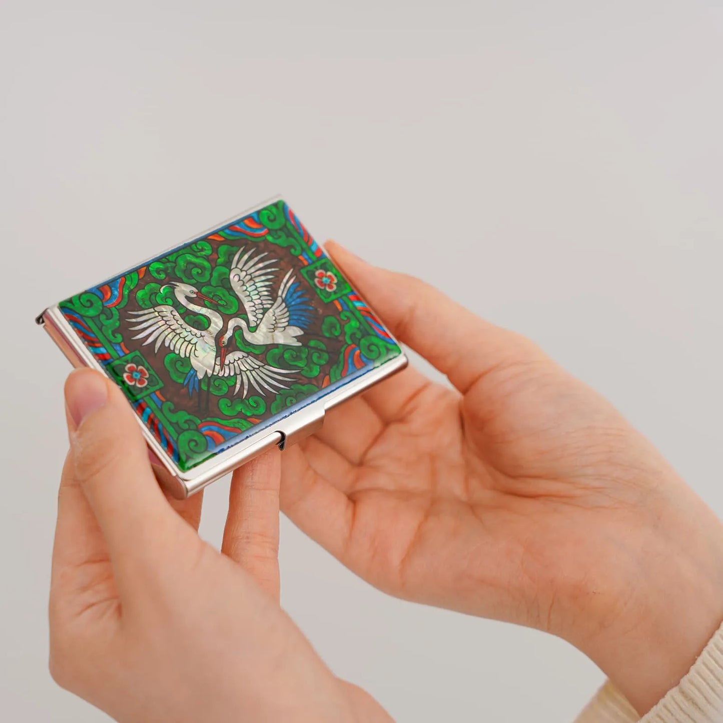 Hands holding a card case with a vibrant design of twin white cranes