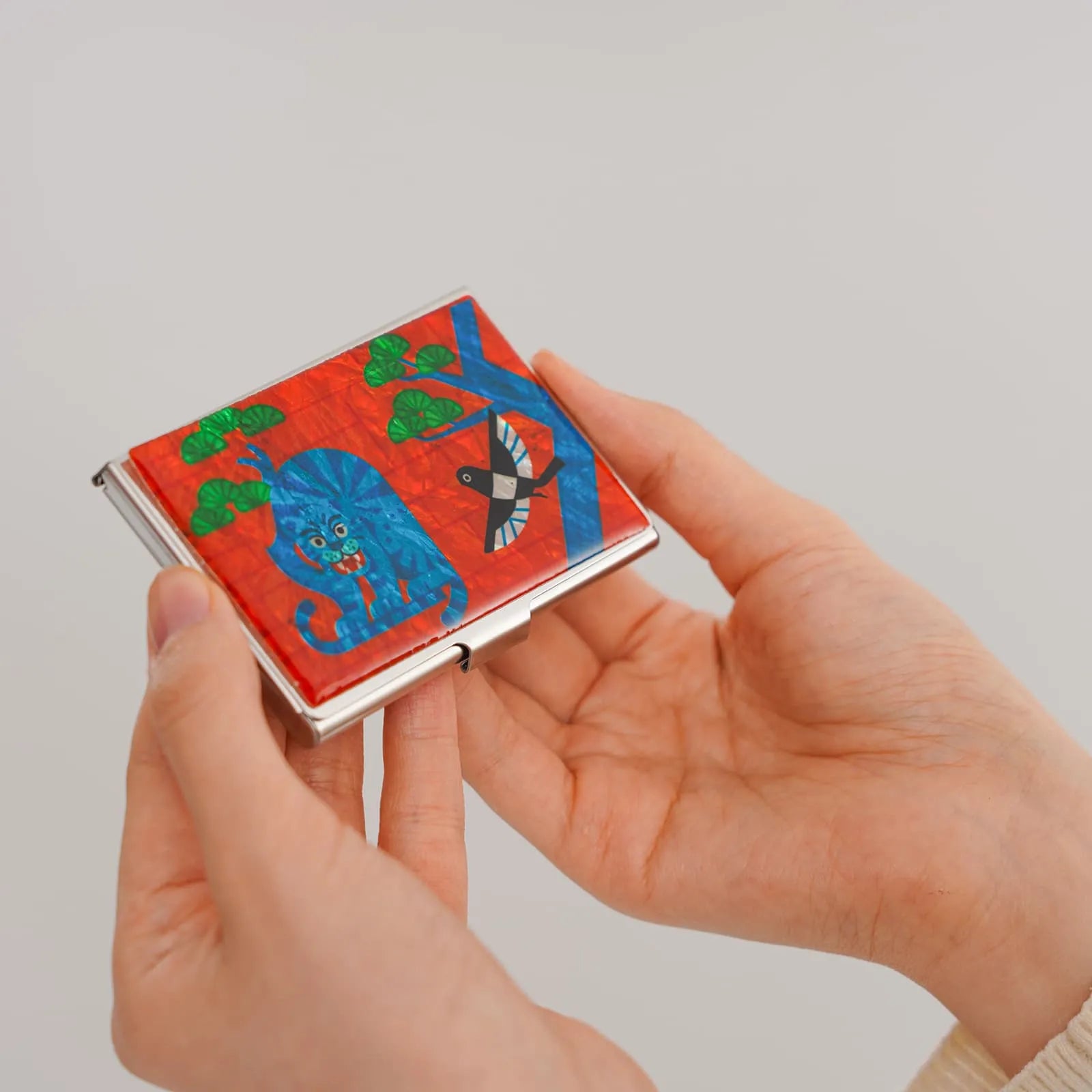 Hands holding a card case with vibrant traditional Korean animal artwork
