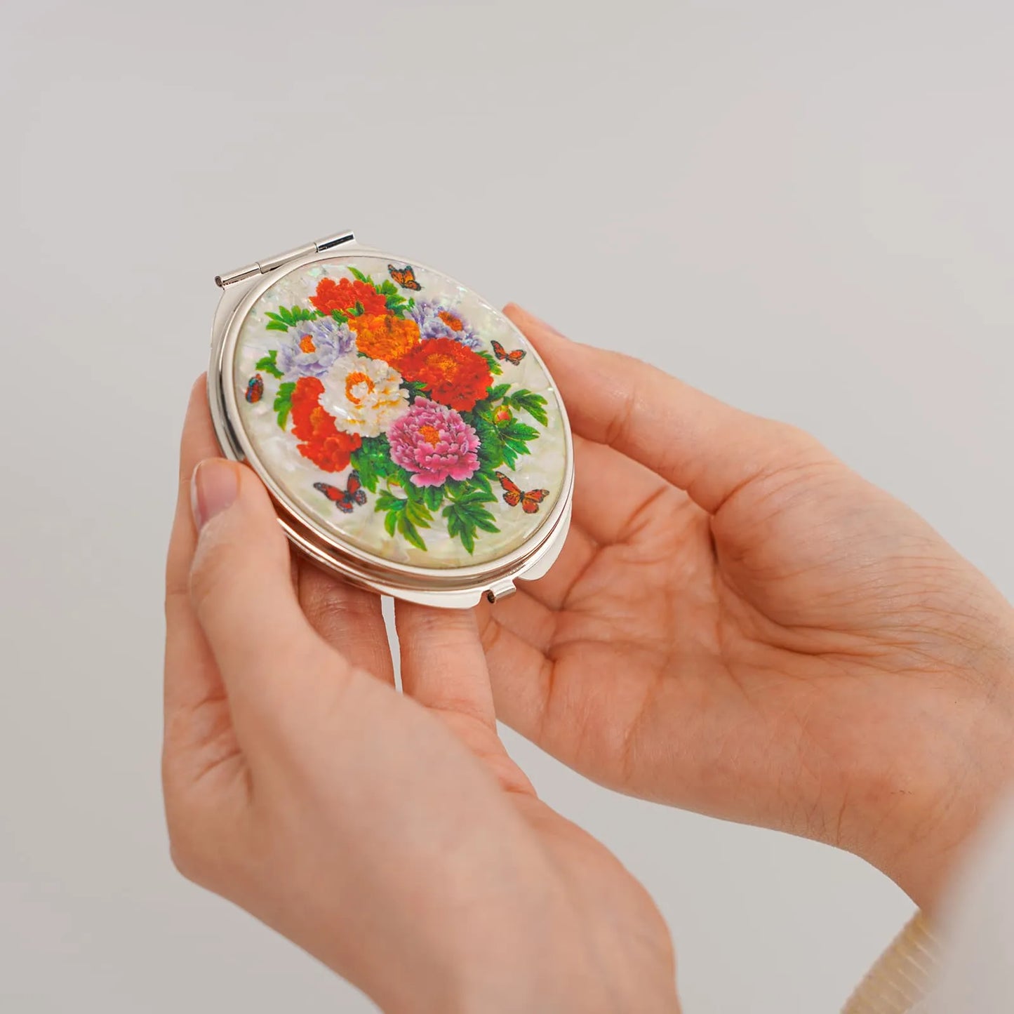 Hands holding a compact mirror with mother-of-pearl floral inlay
