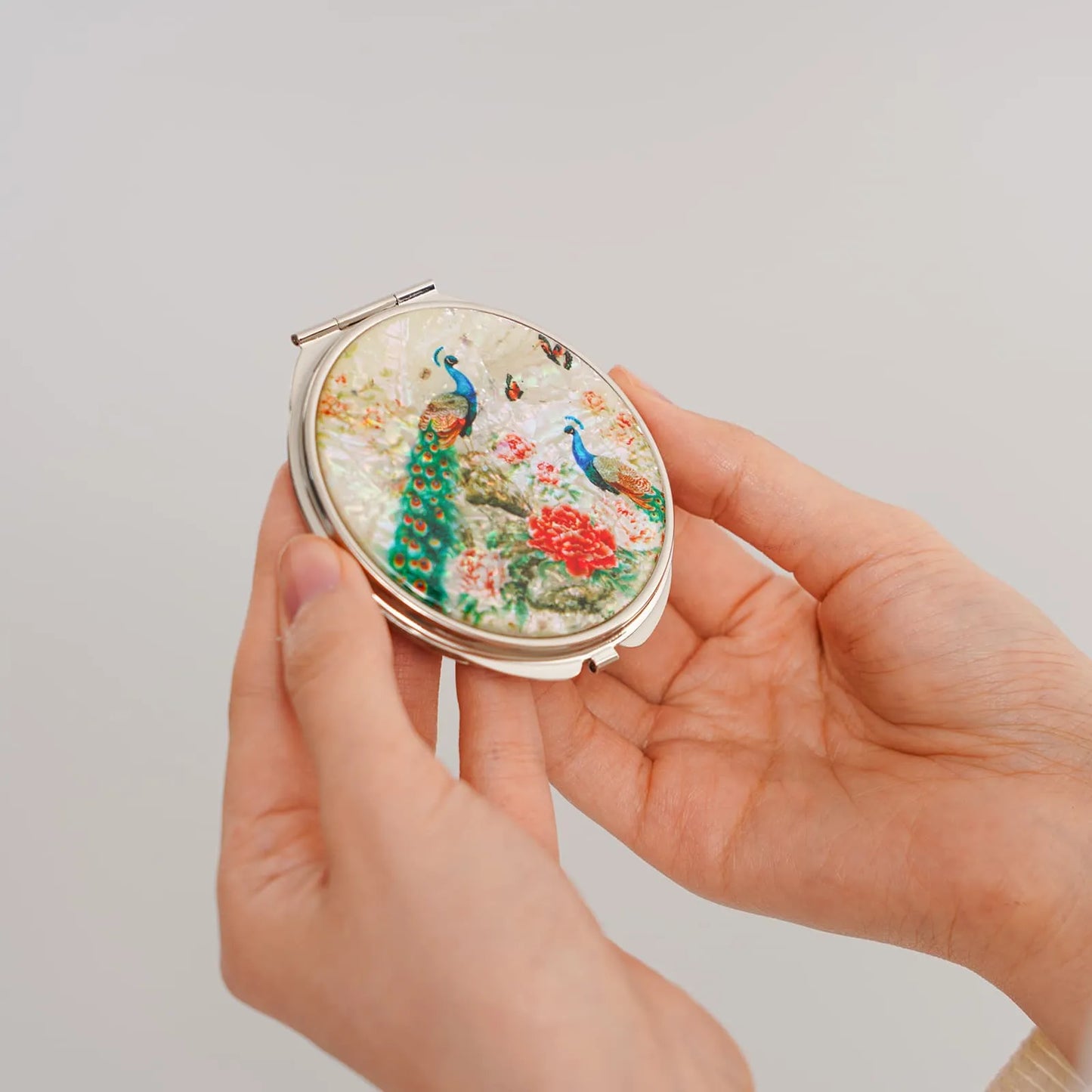 Hands holding a round compact mirror with peacocks and floral mother-of-pearl inlay