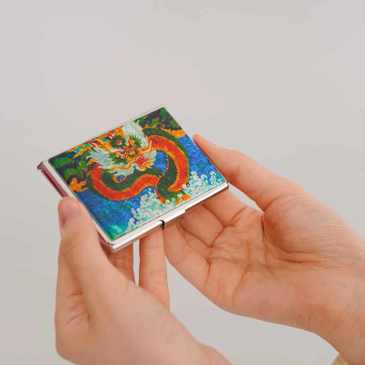 Hands holding a vivid dragon-themed card case with detailed mother-of-pearl inlay.
