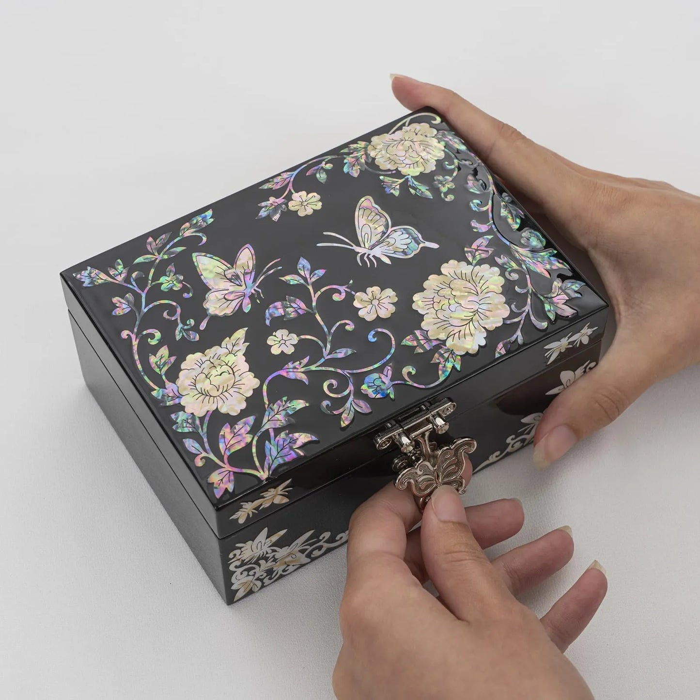 Hands unlocking a black lacquer jewelry box decorated with pearl inlay flowers and butterflies