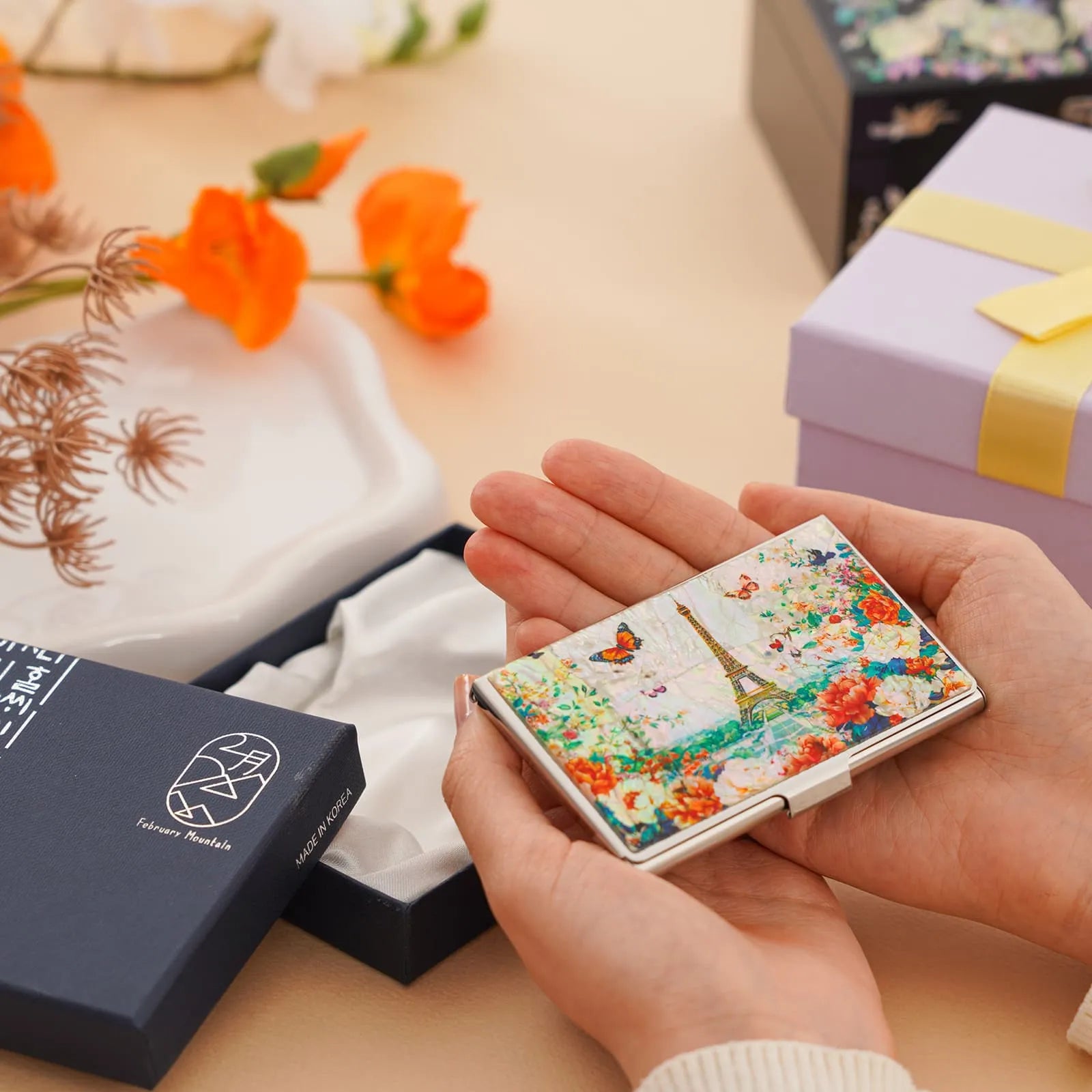 Holding a floral Eiffel Tower card case next to an open gift box and flower decor