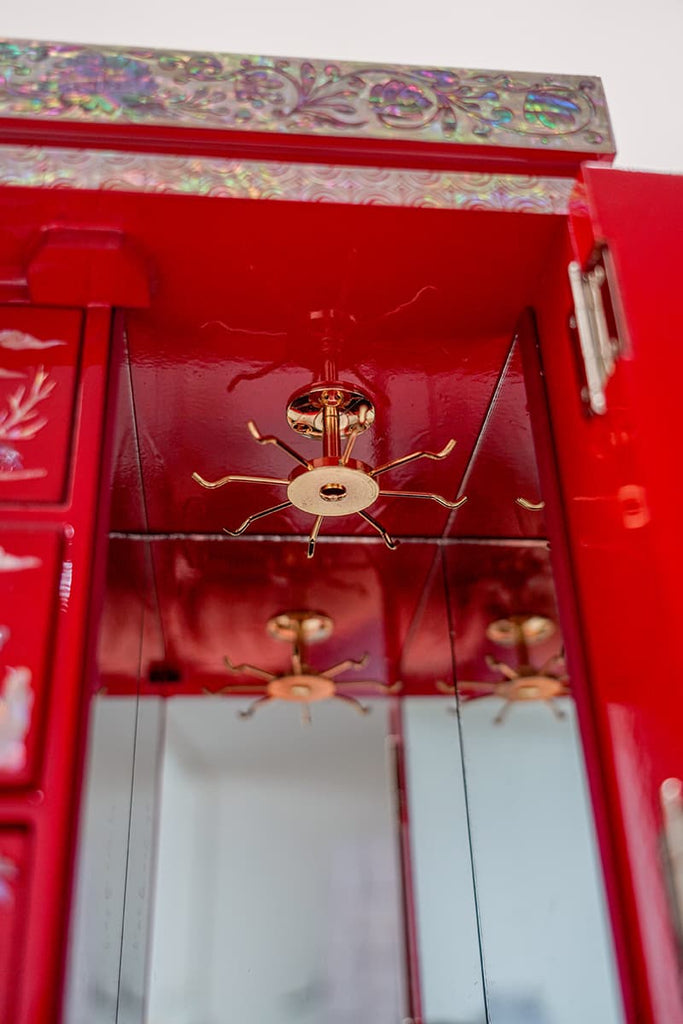 Interior view of a red cabinet with a mirrored back and hanging brass hardware, reflecting a mother of pearl inlaid top.