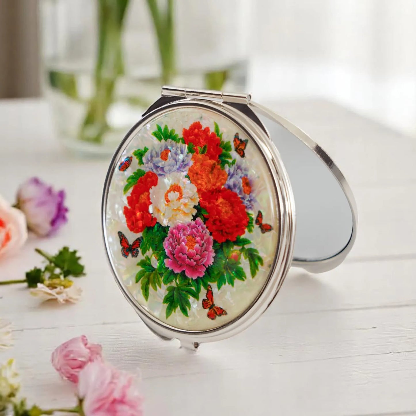Mother-of-pearl compact mirror with vivid peony design on a festive table