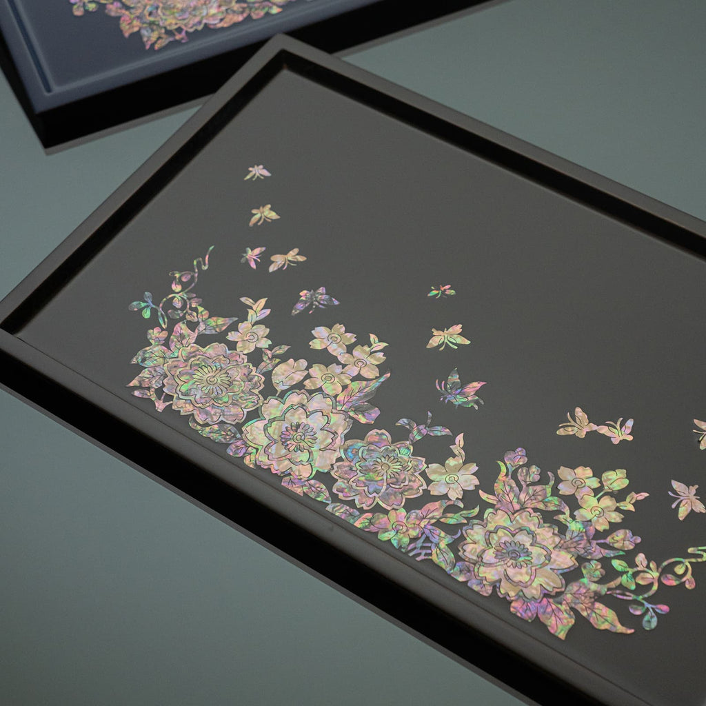 Overlapping dark trays with lustrous Mother of Pearl inlay of flowers and butterflies, one tray is in focus with a clear view of the intricate design.