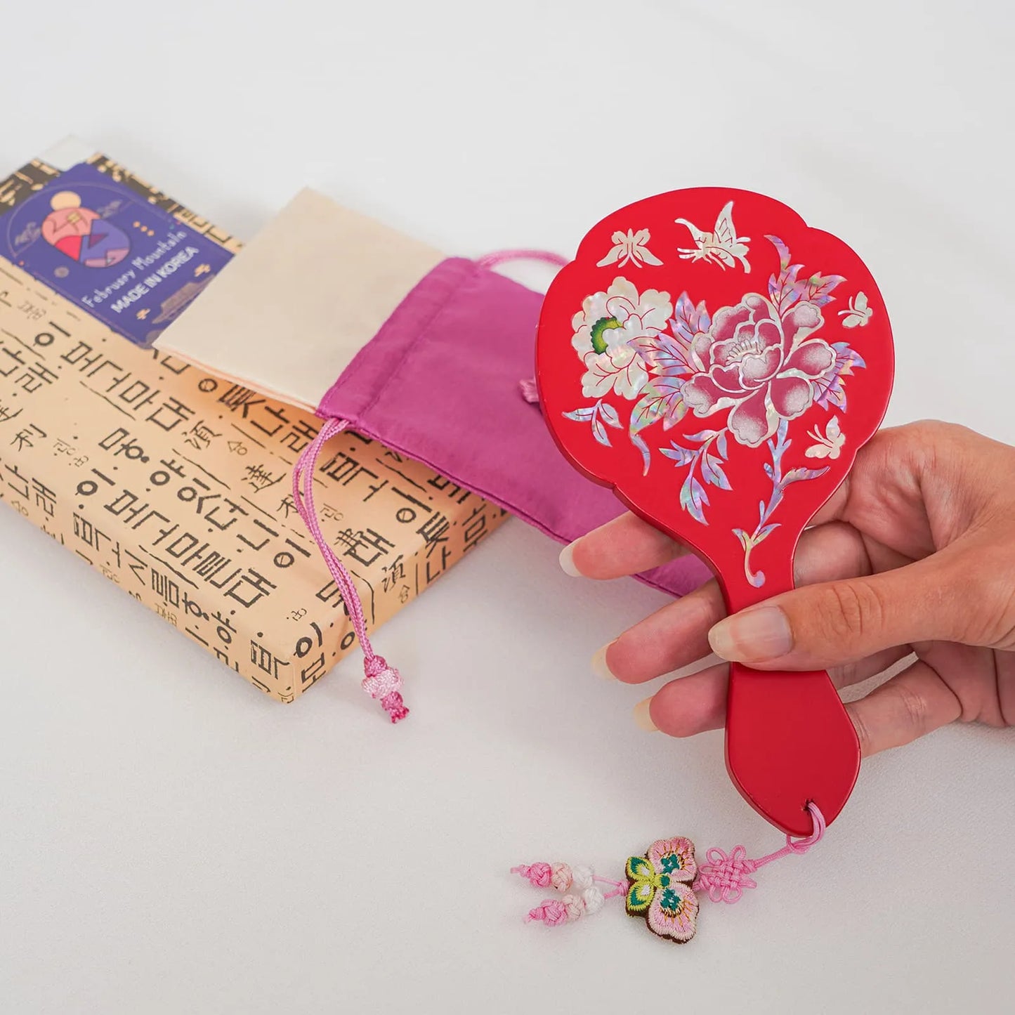 Red hand mirror with peony and butterfly inlay, shown with pouch and gift box