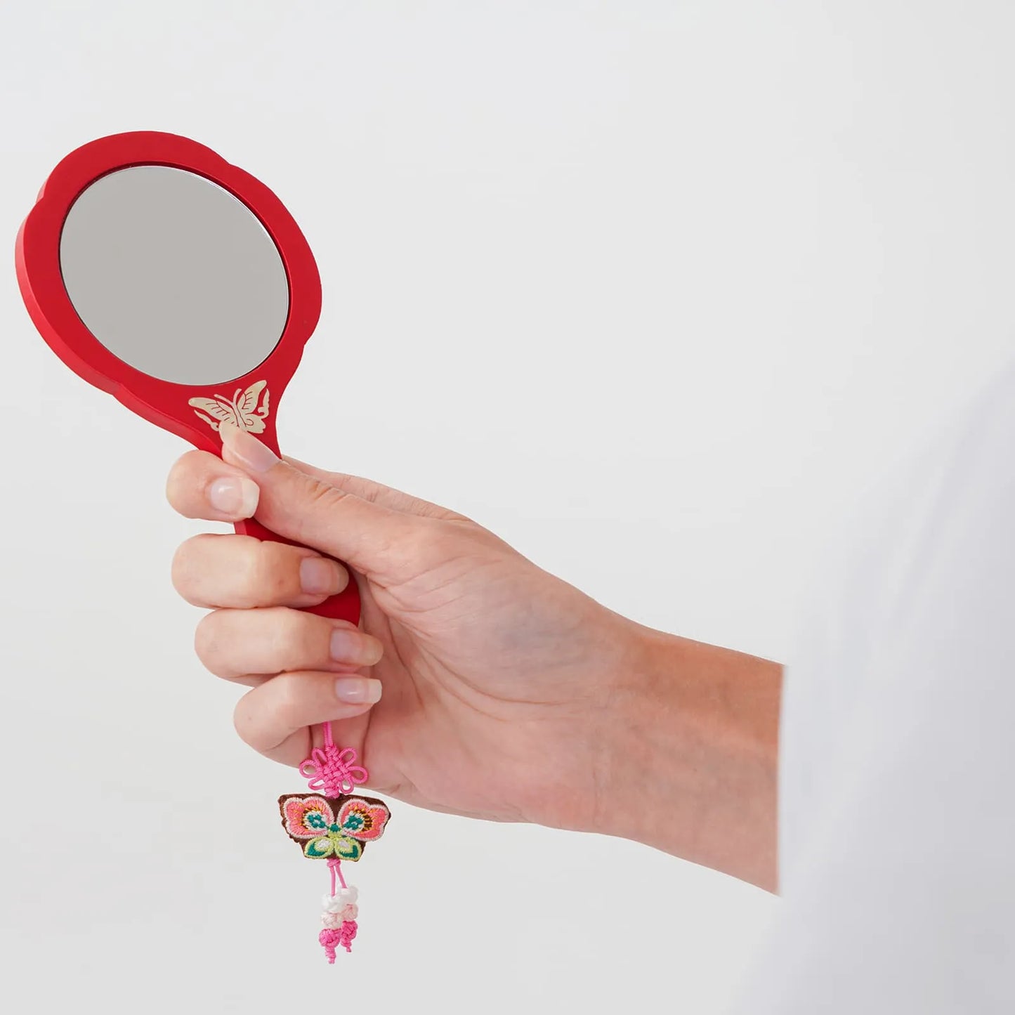 Red mirror with butterfly detail, held in hand with pink tassel