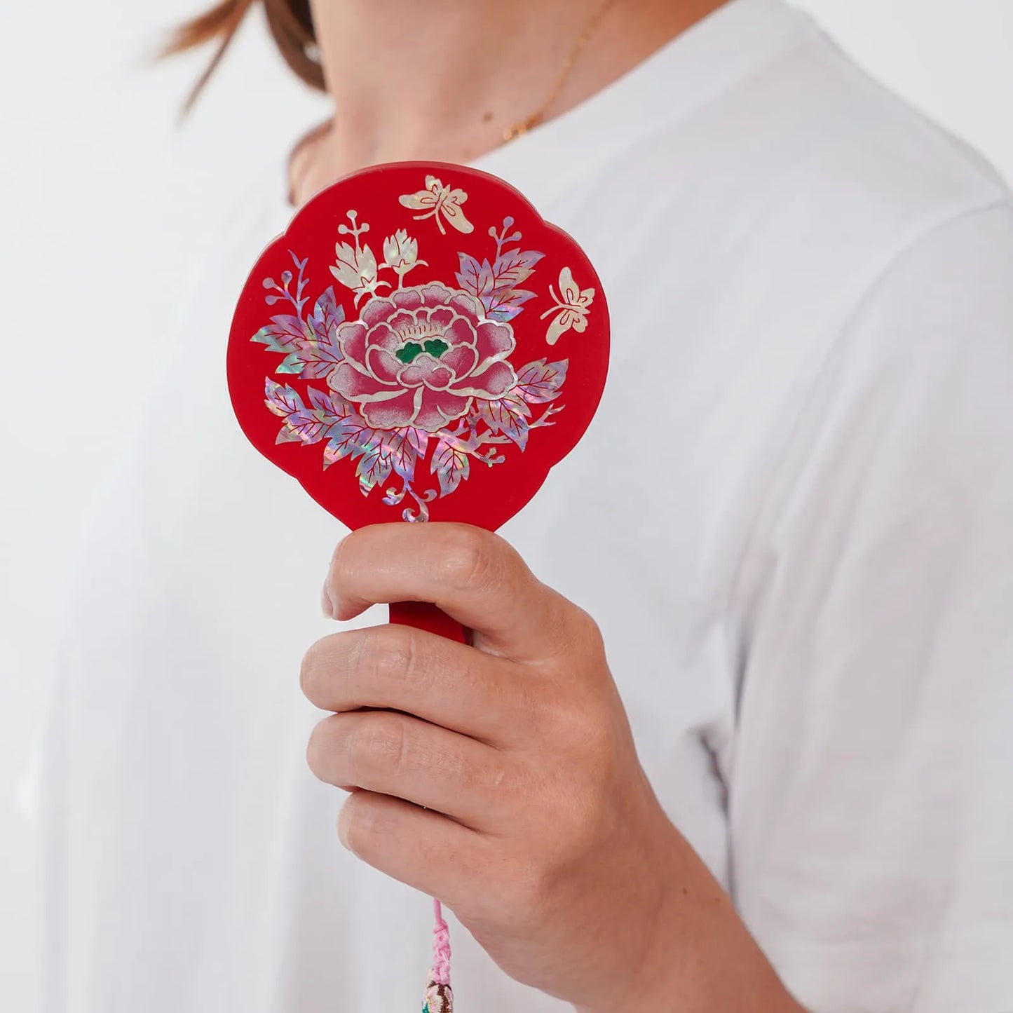 Red mirror with mother-of-pearl peony and butterflies, held in hand