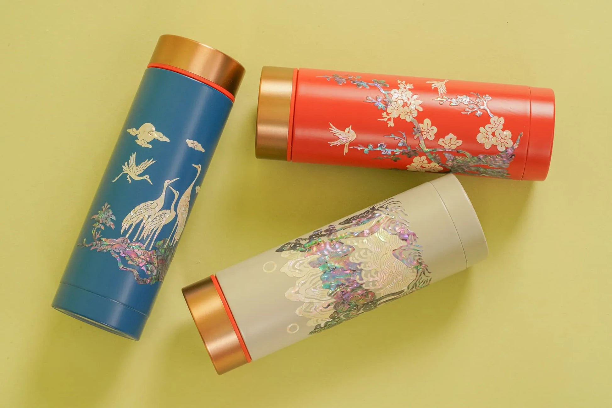 Three tumblers with mother-of-pearl patterns lying on yellow surface, top view