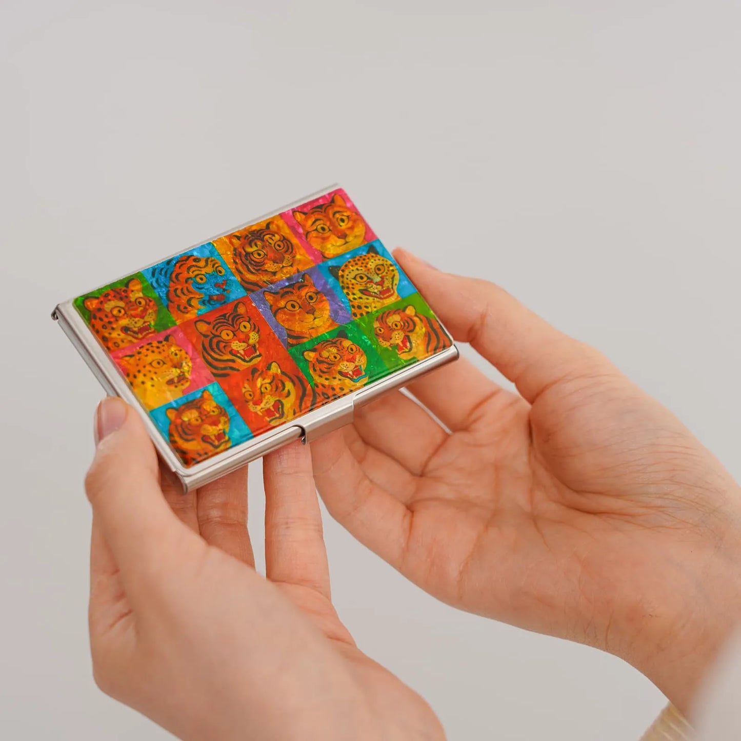 Two hands holding a vivid tiger face design card holder