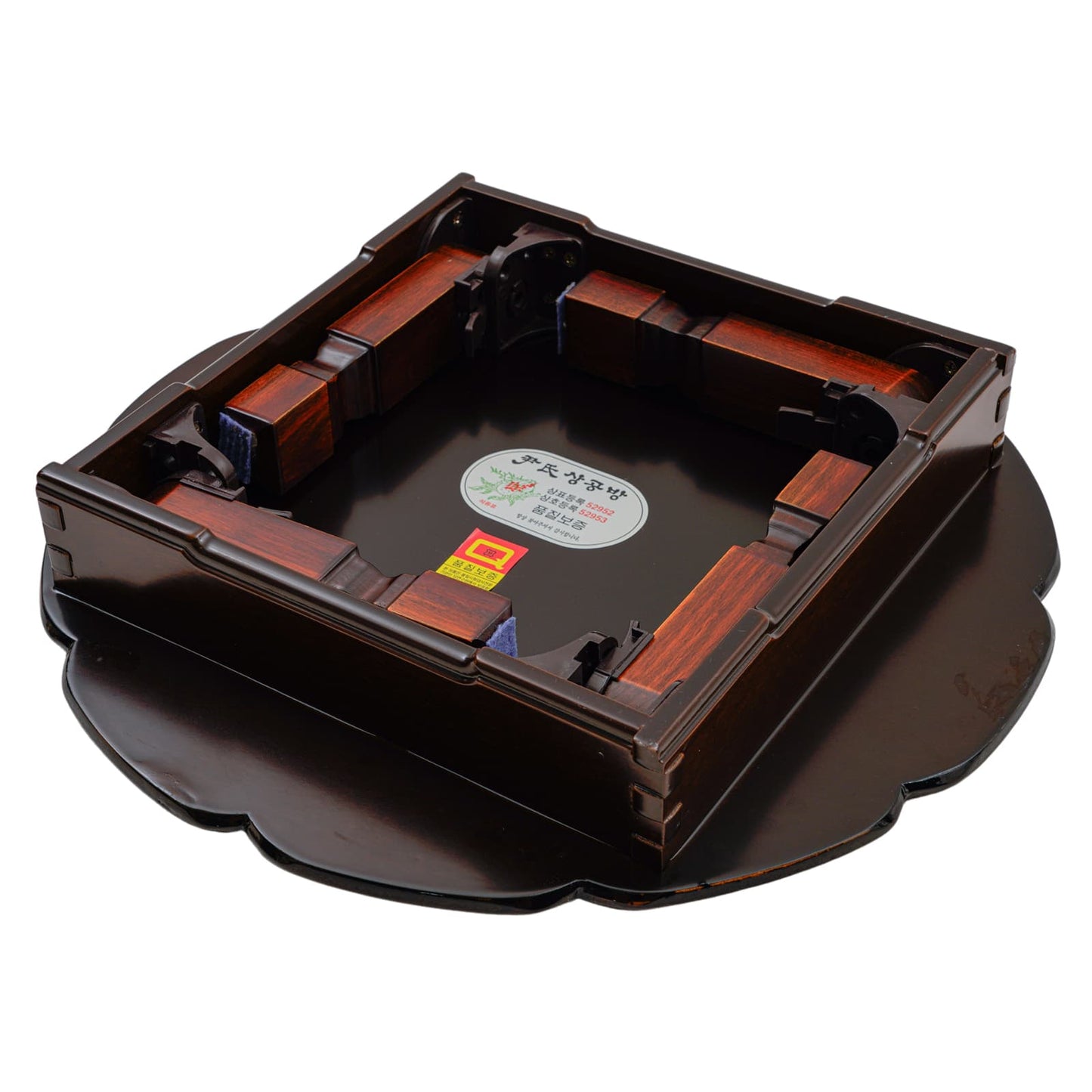 Underside view of a red scalloped-edge lacquered tray showing intricate wooden leg supports and labels.