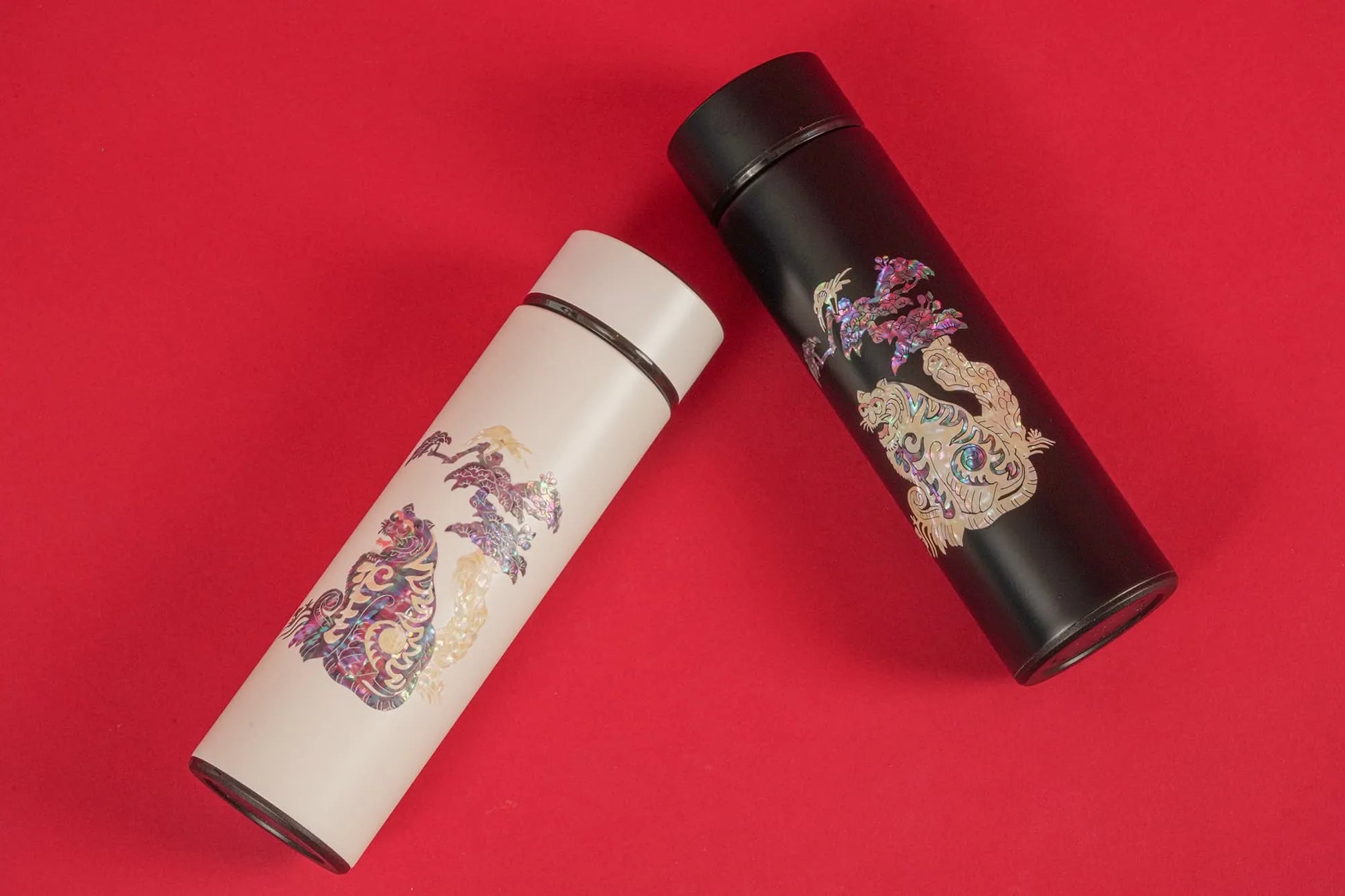 White and black tumblers with tiger design lying diagonally on red background