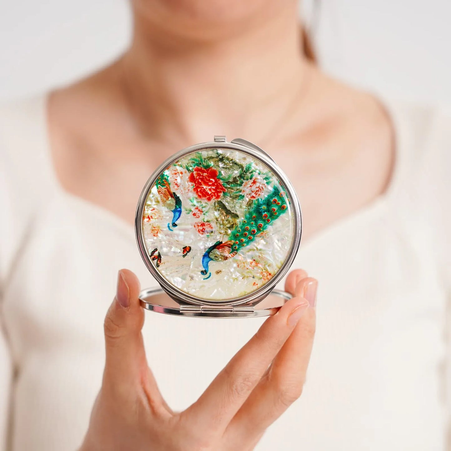 Woman holding compact mirror with colorful peacock and flower inlay