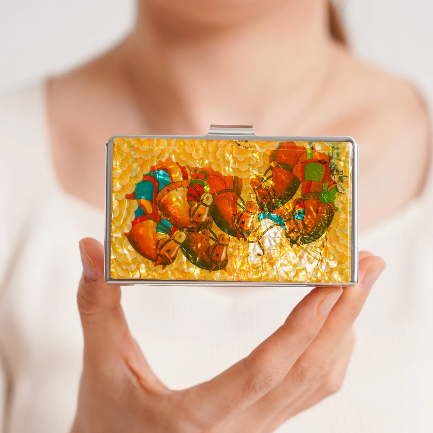 Woman holding iridescent card case featuring horses in warm golden tones