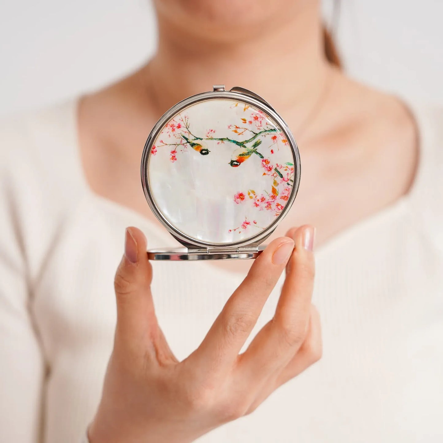 Woman holding open compact mirror with cherry blossom design