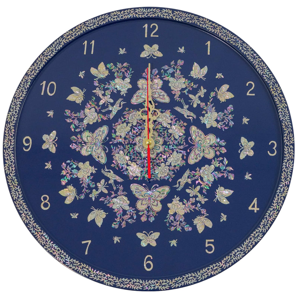 Elegant wall clock with a navy blue background, adorned with a mother of pearl design featuring butterflies and flowers, and gold hands centered over the design. The clock is bordered by a detailed leaf pattern.