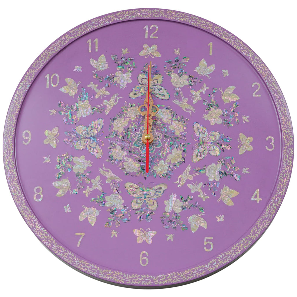 Ornamental wall clock featuring a lilac purple background with a mother of pearl inlay design depicting butterflies and floral patterns, complete with gold-toned hands. The clock face is framed by a delicate vine motif around the edge.