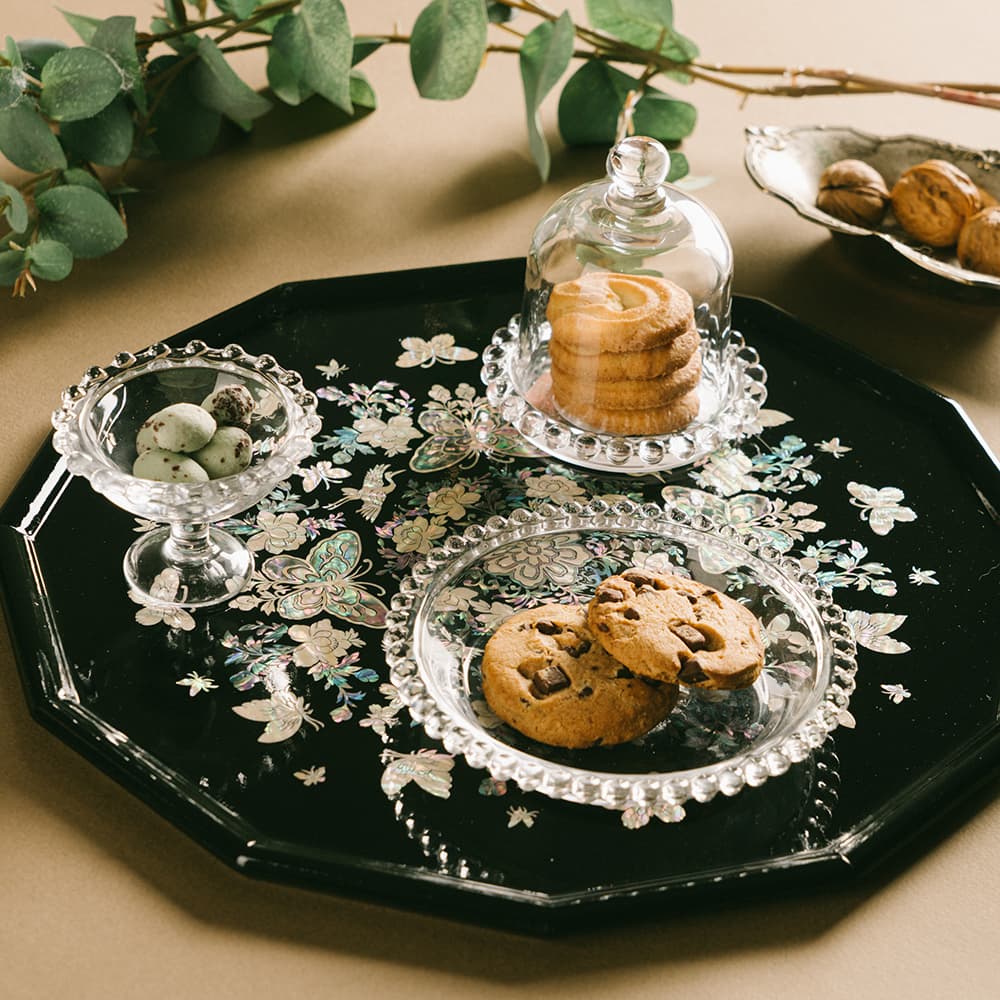 A black octagonal mother-of-pearl tray adorned with cookies and sweets, elegantly presented with glass dessert stands.