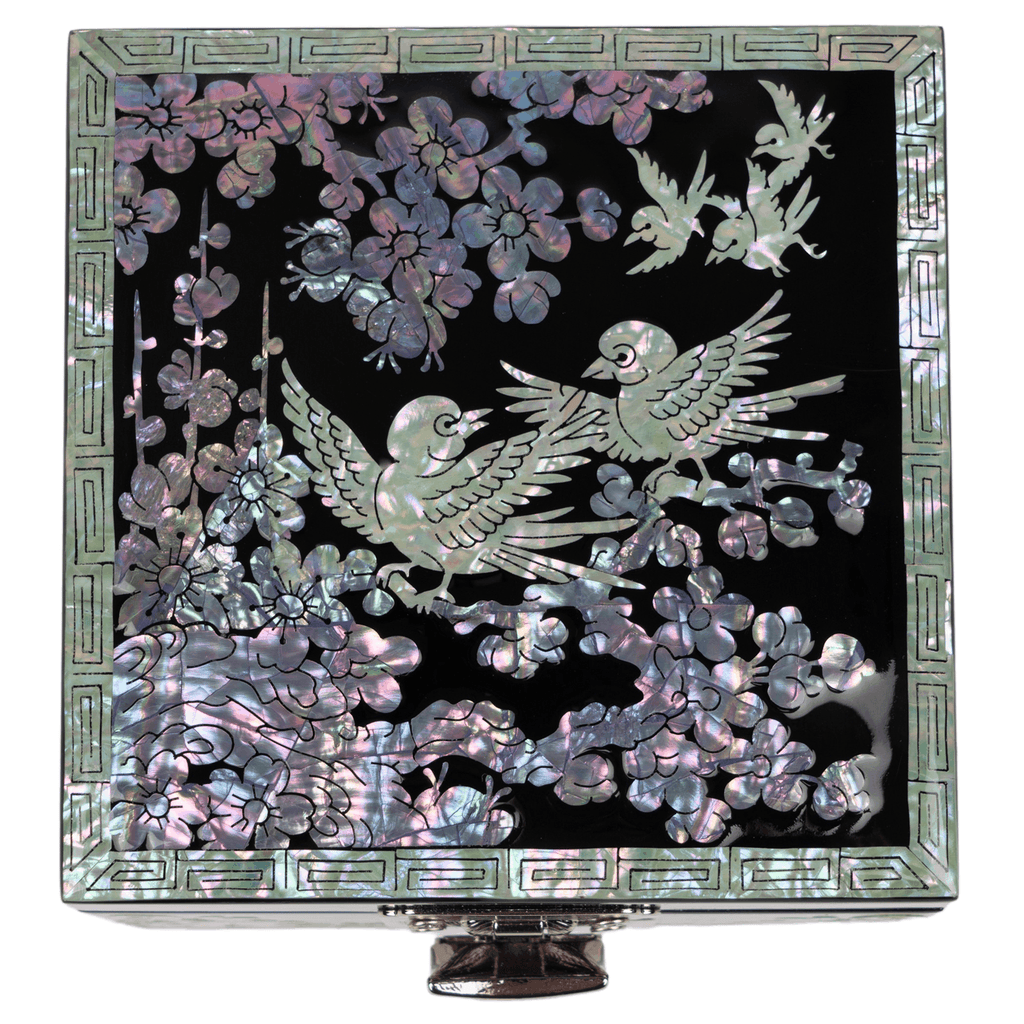 A jewelry box featuring a mother-of-pearl design with birds and flowers on a black background, bordered by a geometric frame, standing on a pedestal base.