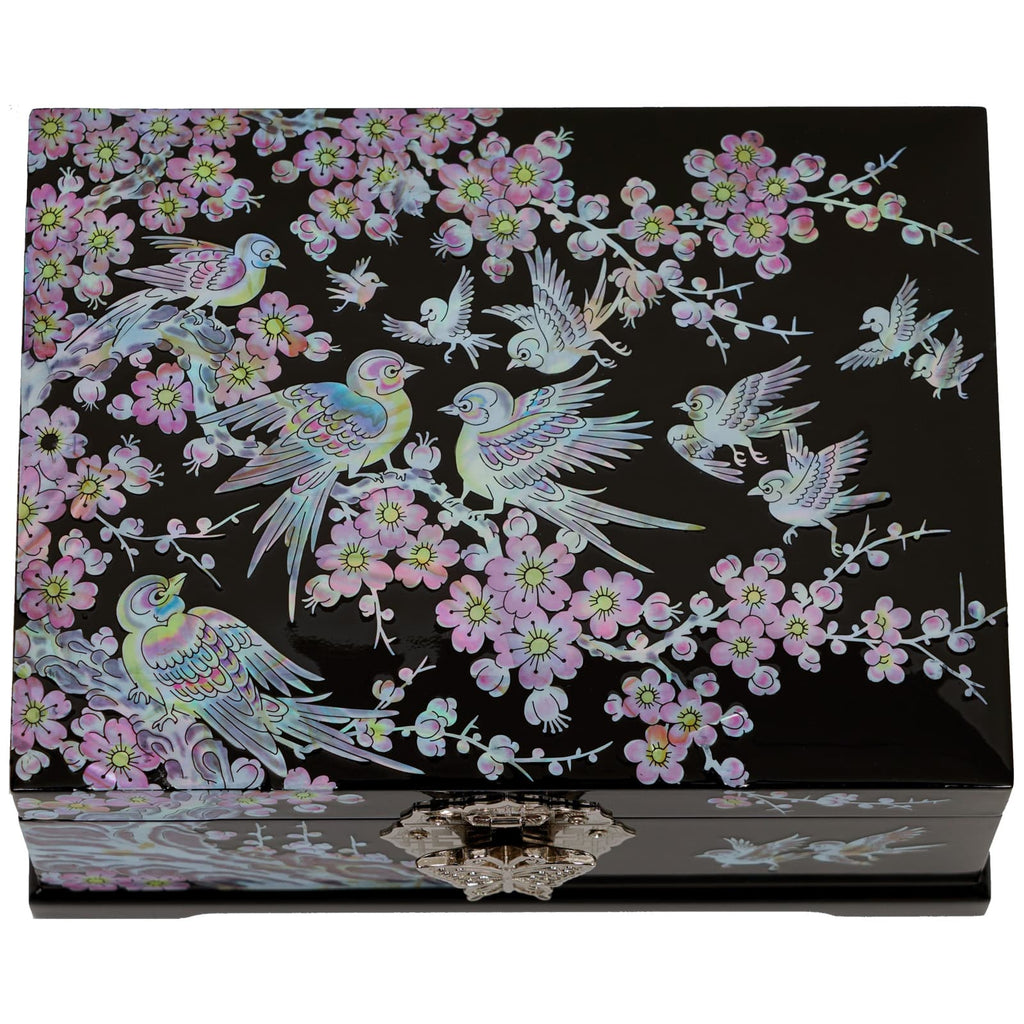 A black lacquered box adorned with a mother of pearl inlay depicting a scene of birds in flight amongst branches of a plum blossom tree, with intricate detailing and a metallic clasp.