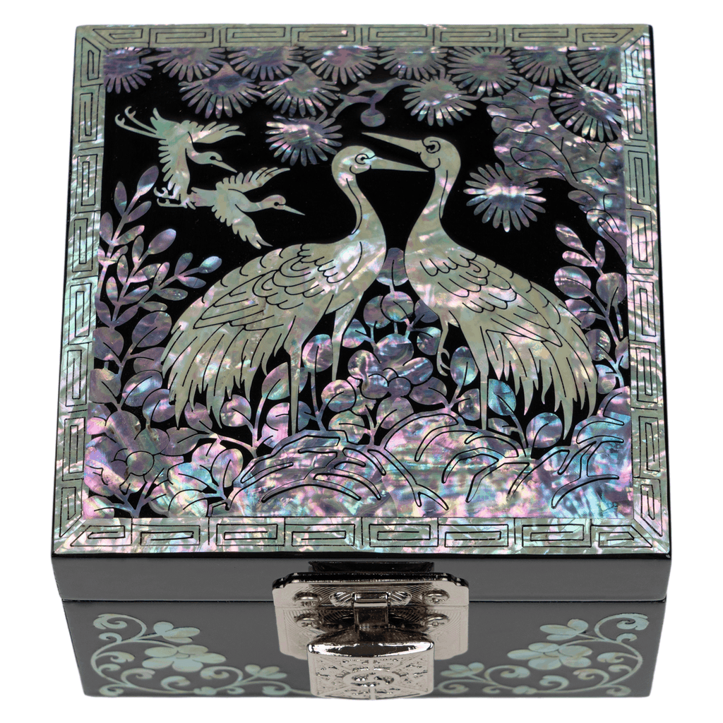A jewelry box with a mother-of-pearl inlay of cranes and florals on a black background, framed by a geometric border, with a silver clasp at the front.
