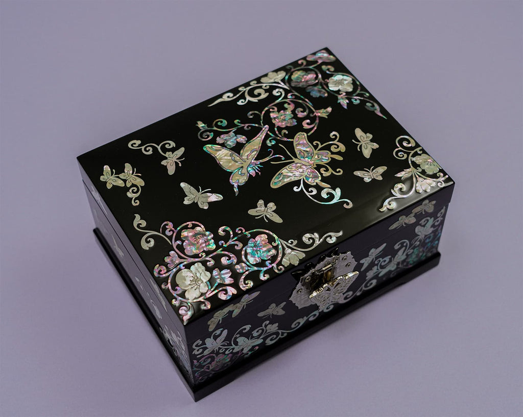 A black jewelry box with mother-of-pearl inlays featuring butterflies and floral designs, displayed on a purple background.