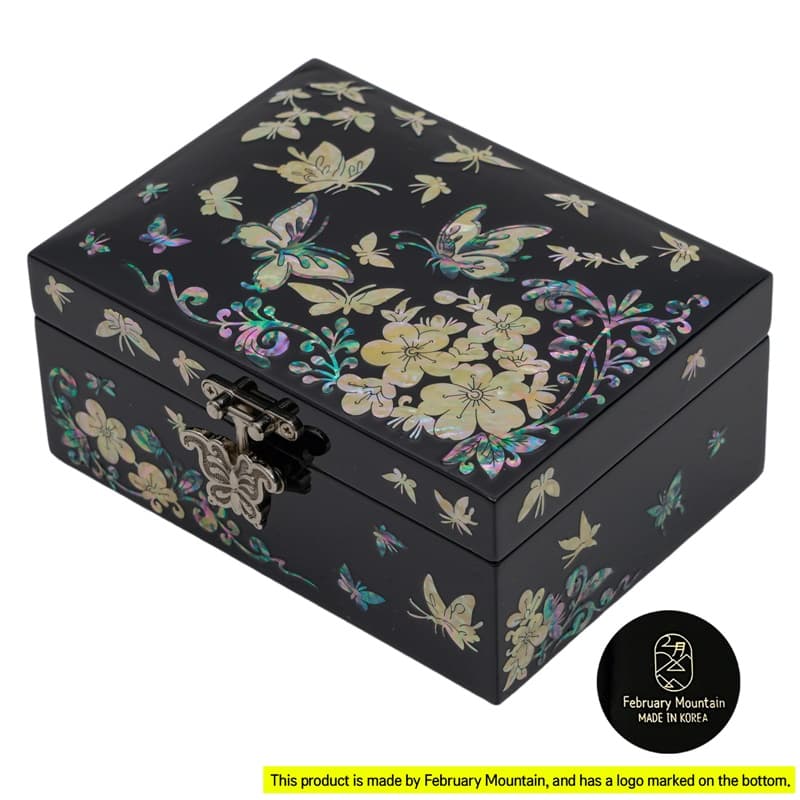 A black lacquer box with mother-of-pearl floral and butterfly inlays, featuring a metal clasp, crafted by February Mountain, marked with their logo on the bottom, made in Korea.