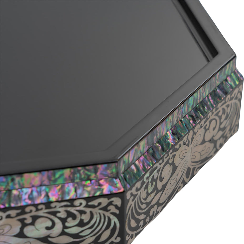 A close-up of an octagonal black lacquer box's edge, showing the shimmering Mother of Pearl inlay and intricate floral patterns against a dark background.